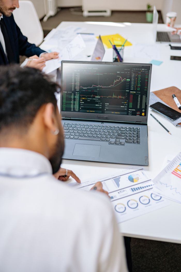 Home Business professionals analyzing stock charts and graphs on a laptop in an office setting.
